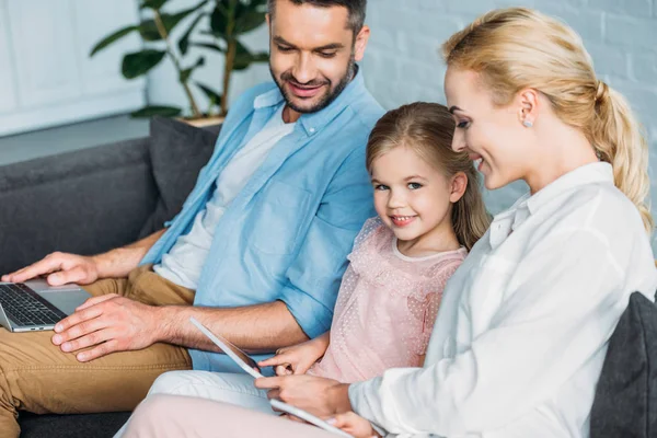 Glückliche Familie nutzt digitale Geräte, während sie zu Hause auf dem Sofa sitzt — Stockfoto