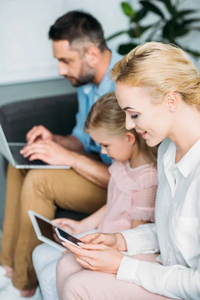 Familia con un niño usando aparatos mientras están sentados juntos en casa - foto de stock