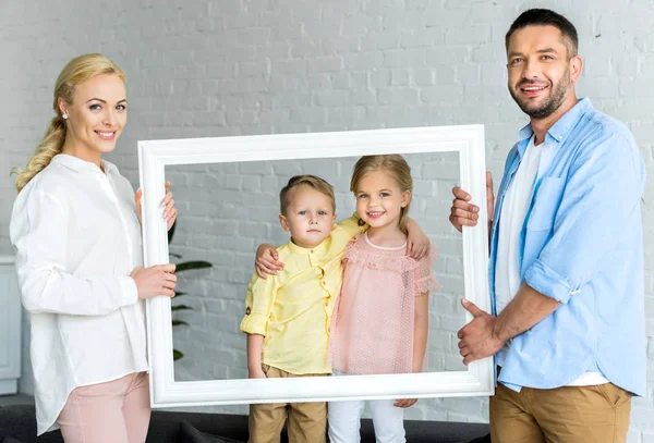 Happy parents holding frame and cute little children smiling at camera — Stock Photo
