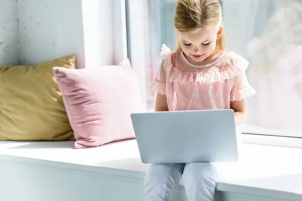 Entzückendes kleines Kind, das auf der Fensterbank sitzt und Laptop benutzt — Stockfoto