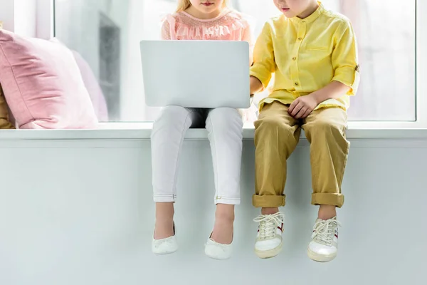 Cropped shot of little kids sitting on windowsill and using laptop — Stock Photo