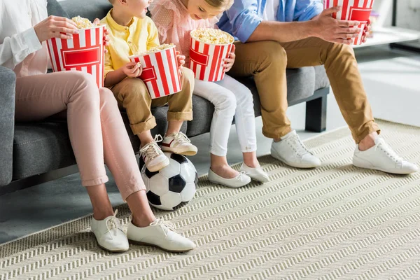 Cropped shot of family eating popcorn while sitting on sofa with soccer ball — Stock Photo