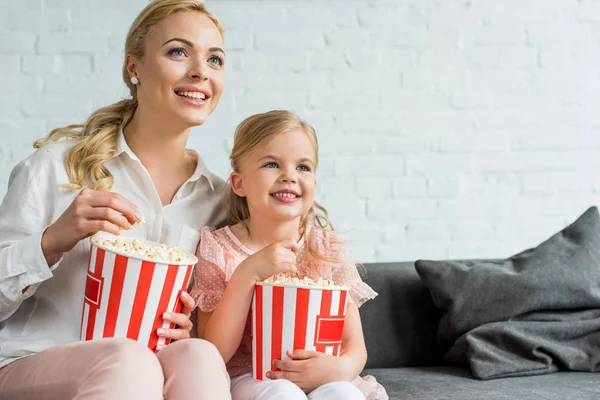 Happy mother and daughter eating popcorn and looking away at home — Stock Photo