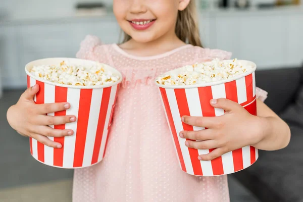 Cropped shot of cute smiling child holding popcorn boxes at home — Stock Photo