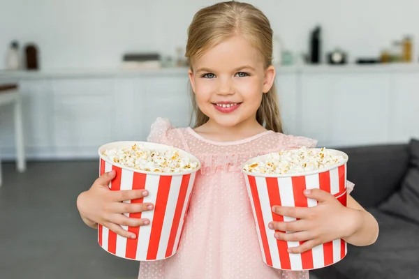 Adorabile bambino che tiene scatole con popcorn e sorridente alla macchina fotografica — Foto stock