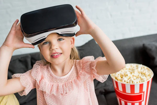 Adorable child in virtual reality headset smiling at camera at home — Stock Photo