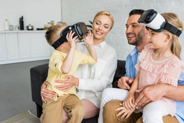 Happy parents looking at cute little kids using virtual reality headsets at home — Stock Photo