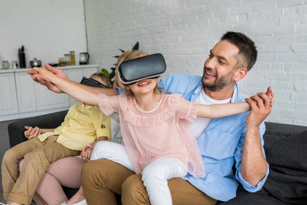 Pais felizes brincando com crianças usando fones de ouvido realidade virtual em casa — Fotografia de Stock