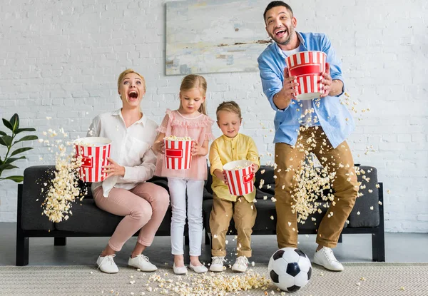 Famiglia eccitata con due bambini che tengono scatole e gettano popcorn a casa — Foto stock