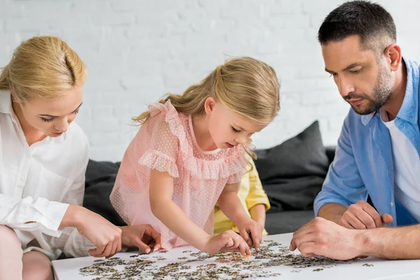 Padres con linda hijita jugando con piezas de rompecabezas en casa - foto de stock