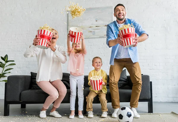 Aufgeregte Familie hält Kisten in der Hand und wirft Popcorn nach Hause — Stockfoto