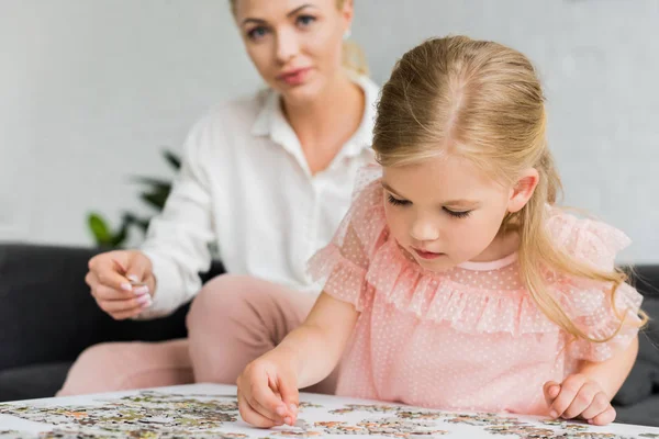 Adorable little child playing with puzzle pieces while mother sitting behind — Stock Photo