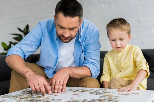 Padre y lindo hijo pequeño jugando con rompecabezas juntos en casa - foto de stock