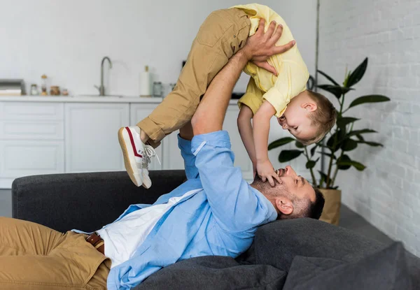 Vista laterale di padre e figlio felici che si divertono insieme sul divano di casa — Foto stock