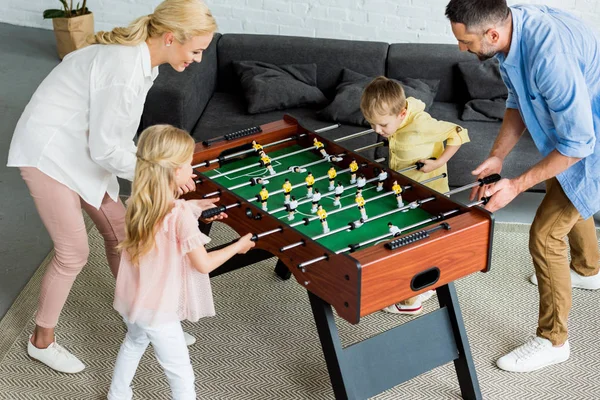 Високий кут зору щасливої сім'ї з двома дітьми, які грають у настільний футбол разом вдома — стокове фото
