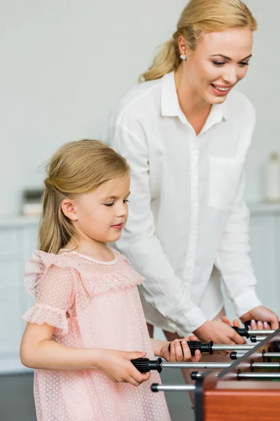 Happy mother and adorable little daughter playing table football at home — Stock Photo