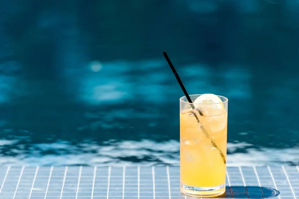 Primo piano colpo di vetro di cocktail arancione saporito su bordo piscina — Foto stock