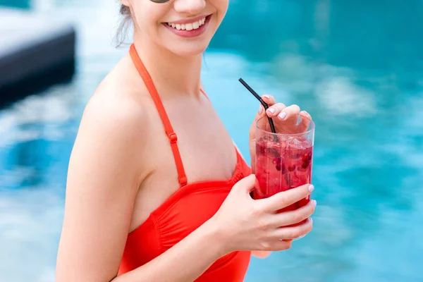 Обрізаний знімок усміхненої молодої жінки з ягідним коктейлем біля басейну — стокове фото