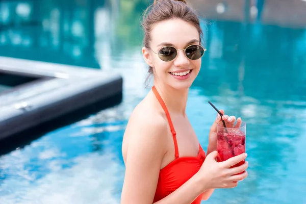 Счастливая молодая женщина в старинных солнцезащитных очках с ягодным коктейлем у бассейна — стоковое фото