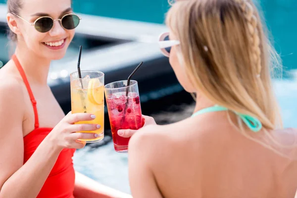 Belles jeunes femmes cliquetis verres de cocktails au bord de la piscine — Photo de stock