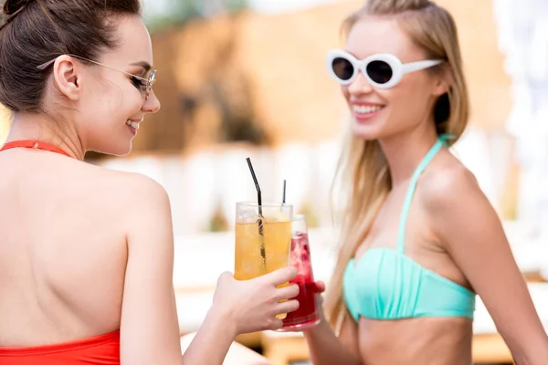 Felices mujeres jóvenes tintineo vasos de cócteles en la piscina - foto de stock