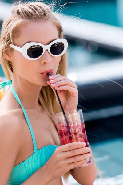 Bella giovane donna in occhiali da sole vintage con cocktail di bacche a bordo piscina — Foto stock