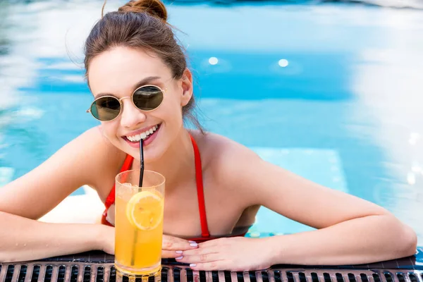 Glückliche junge Frau mit köstlichem Orangencocktail entspannt am Pool — Stockfoto