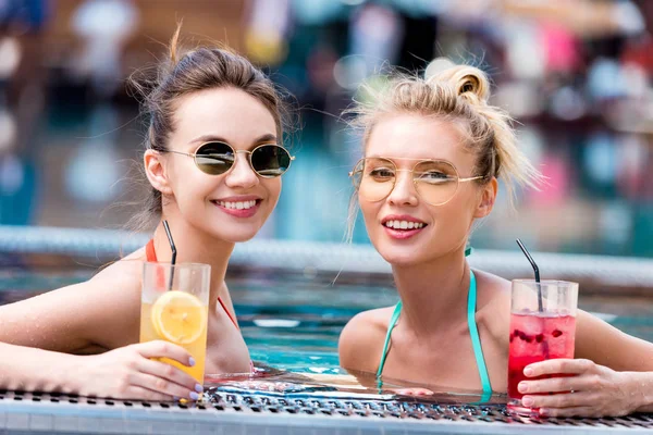 Happy young women with delicious cocktails relaxing in swimming pool — Stock Photo