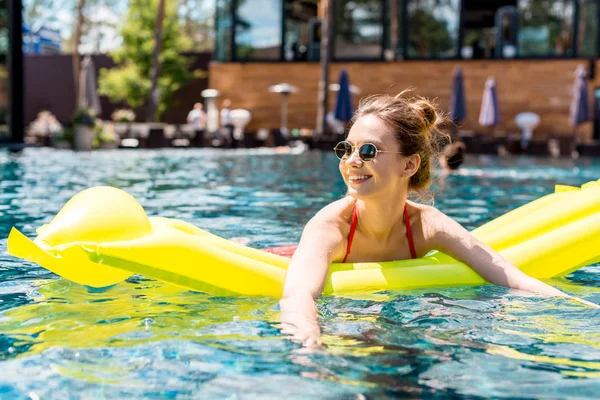 Belle jeune femme couchée sur un matelas gonflable dans la piscine et regardant loin — Photo de stock