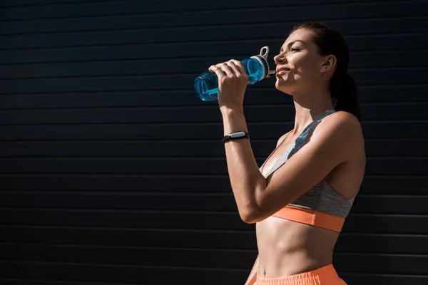 Donna atletica con fitness tracker acqua potabile dalla bottiglia sportiva — Foto stock