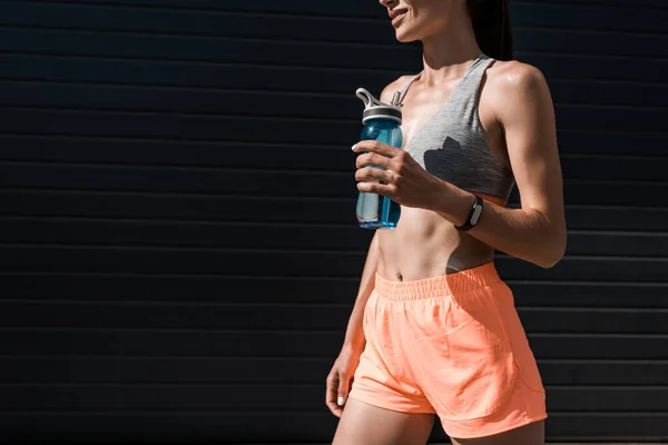 Vista recortada de deportista con rastreador de fitness sosteniendo botella de agua — Stock Photo