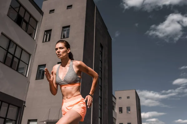 Joven deportista concentrada corriendo con rastreador de fitness en la ciudad - foto de stock