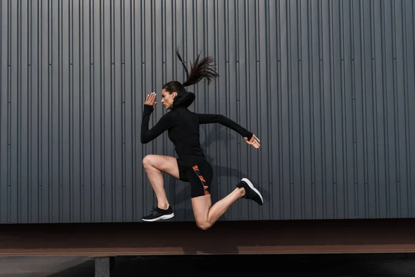 Атлетичная женщина в черной термальной одежде прыгает в городе — стоковое фото