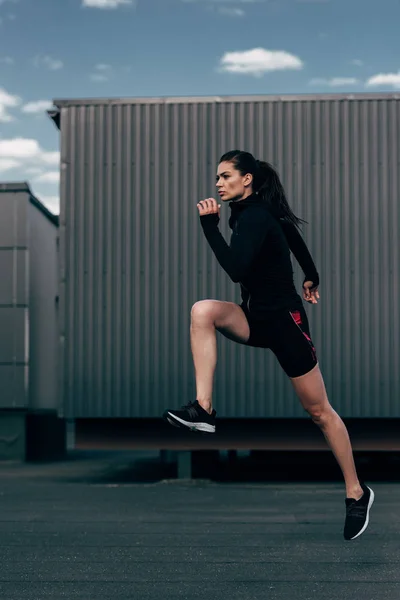 Молодая спортсменка в черной теплой одежде прыгает в город — стоковое фото