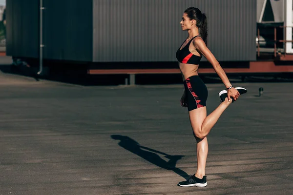 Young sportswoman stretching legs on roof in city — Stock Photo