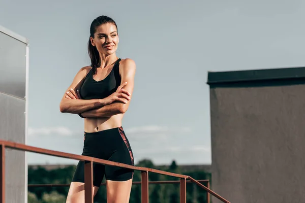 Attractive confident sportswoman with crossed arms posing on roof — Stock Photo