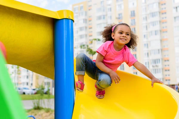 Criança americana africana feliz deslizando para baixo da colina no playground — Fotografia de Stock