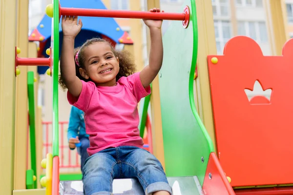 Heureux frisé afro-américain petit enfant glissant vers le bas de colline à aire de jeux — Photo de stock