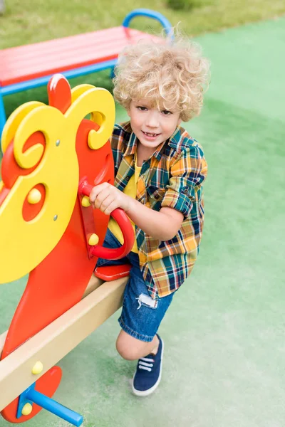 Blick aus der Vogelperspektive auf einen glücklichen Lockenkopf, der auf einem Schaukelpferd auf einem Spielplatz reitet — Stockfoto