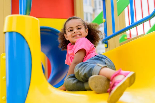 Criança americana africana feliz deslizando para baixo da colina no playground — Fotografia de Stock