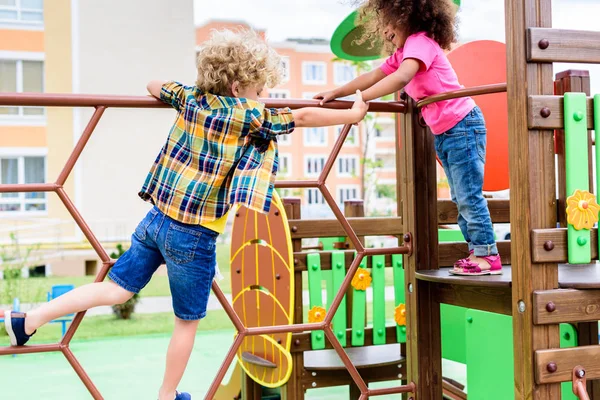 Deux petits enfants multiethniques grimpant et s'amusant à l'aire de jeux — Photo de stock