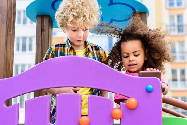 Dos rizado multiétnicos niños pequeños divertirse en el patio de recreo - foto de stock
