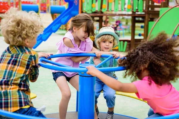 Multiethnic group of little kids riding on carousel at playground — Stock Photo