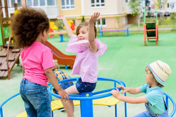 Очаровательная многонациональная группа маленьких детей, катающихся на карусели на детской площадке — стоковое фото