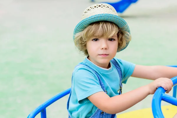 Selective focus of adorable little boy in panama riding on carousel at playground — Stock Photo