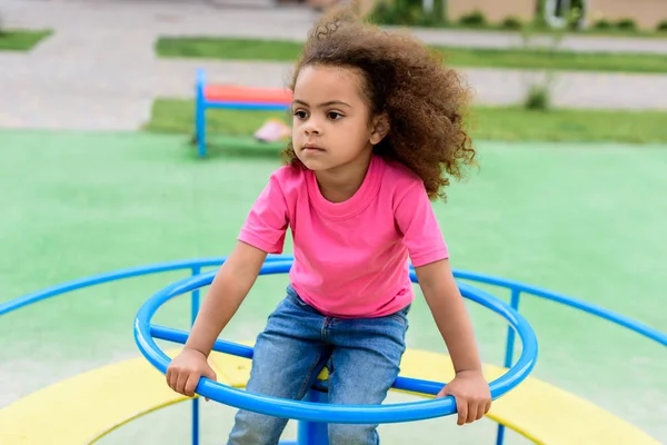 Rizado afroamericano niño pequeño montar en carrusel en el patio de recreo - foto de stock