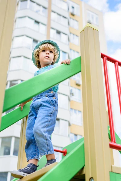 Vue à angle bas du petit garçon au panama descendant à l'aire de jeux — Photo de stock