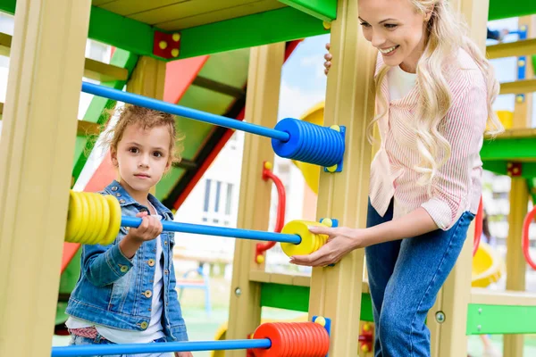 Madre sorridente che insegna a contare la figlioletta su abaco al parco giochi — Foto stock