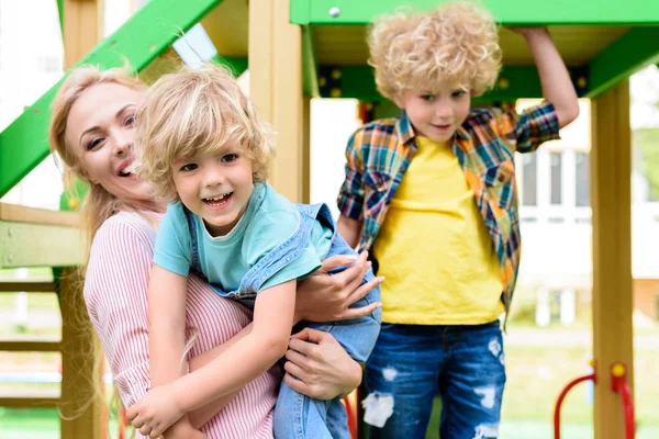 Felice madre con due adorabili bambini giocherelloni al parco giochi — Foto stock