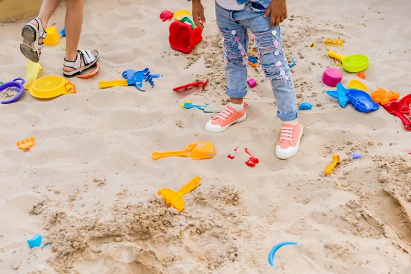 Immagine ritagliata di due bambine in sandbox con palette di plastica, stampi e secchio al parco giochi — Foto stock